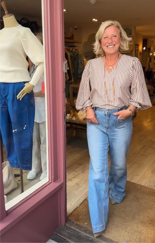 Woman standing in a store doorway wearing a striped shirt and jeans, with mannequins and clothing in the background.