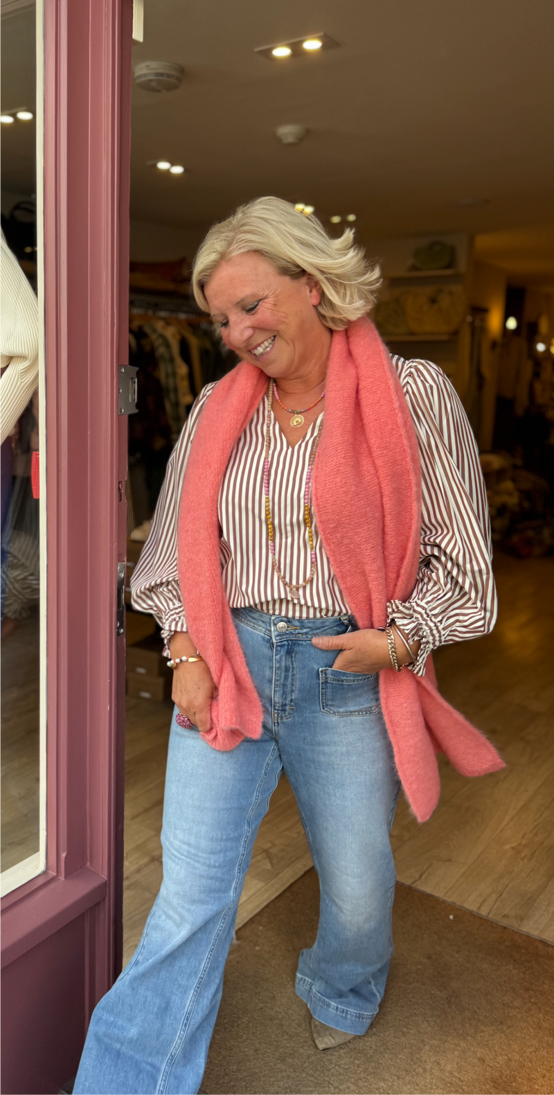 Woman wearing a pink scarf, striped shirt, and jeans in a store setting.