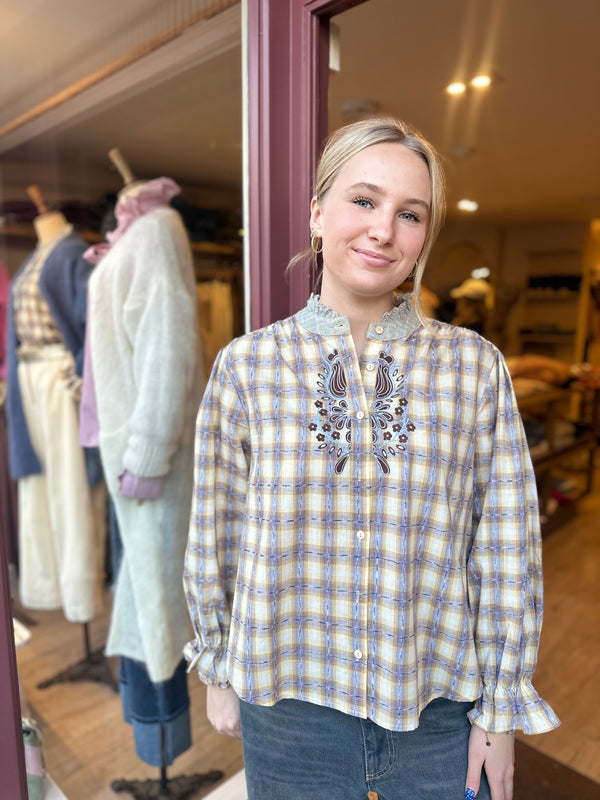 Woman wearing a plaid shirt with floral embroidery in a clothing store.