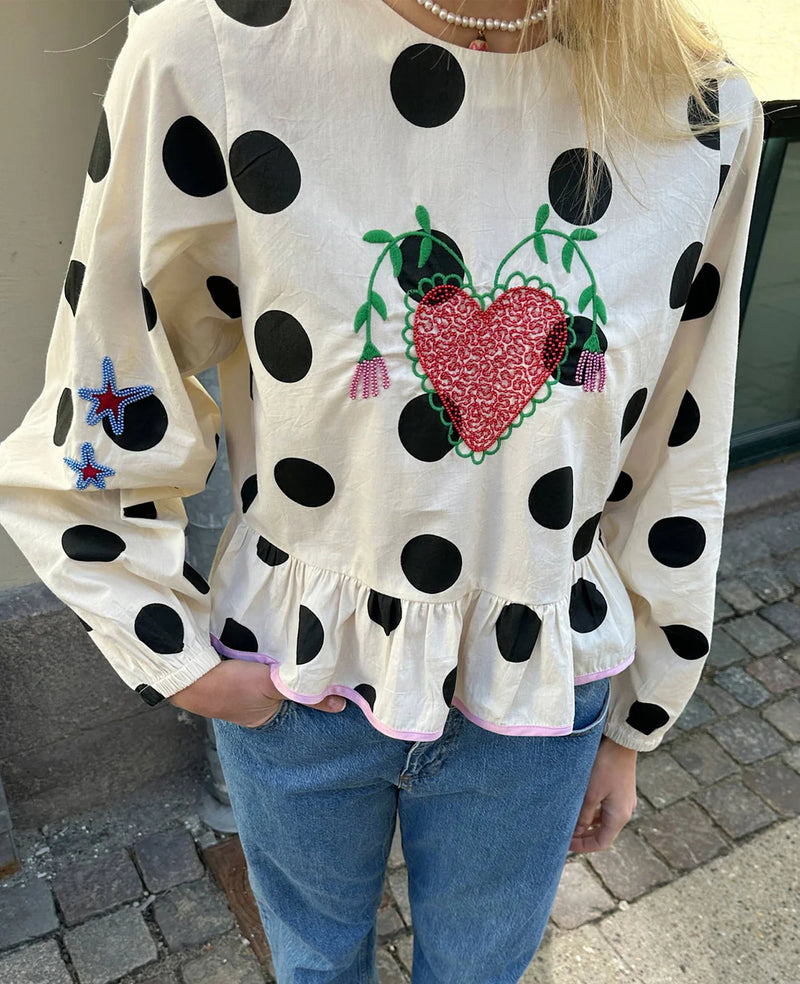 White blouse with black polka dots and a red heart design worn by a person.