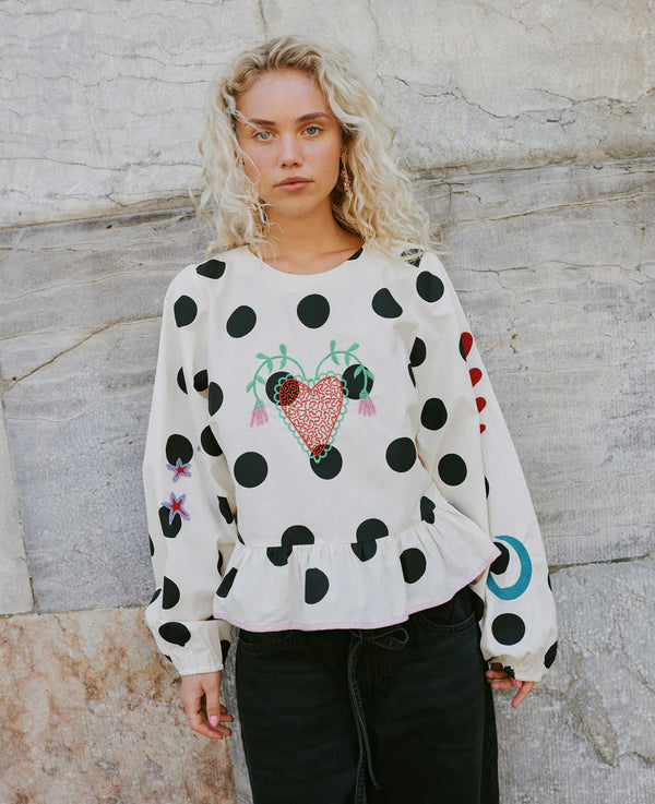 Woman wearing a polka dot sweater with a colorful heart design against a stone wall.