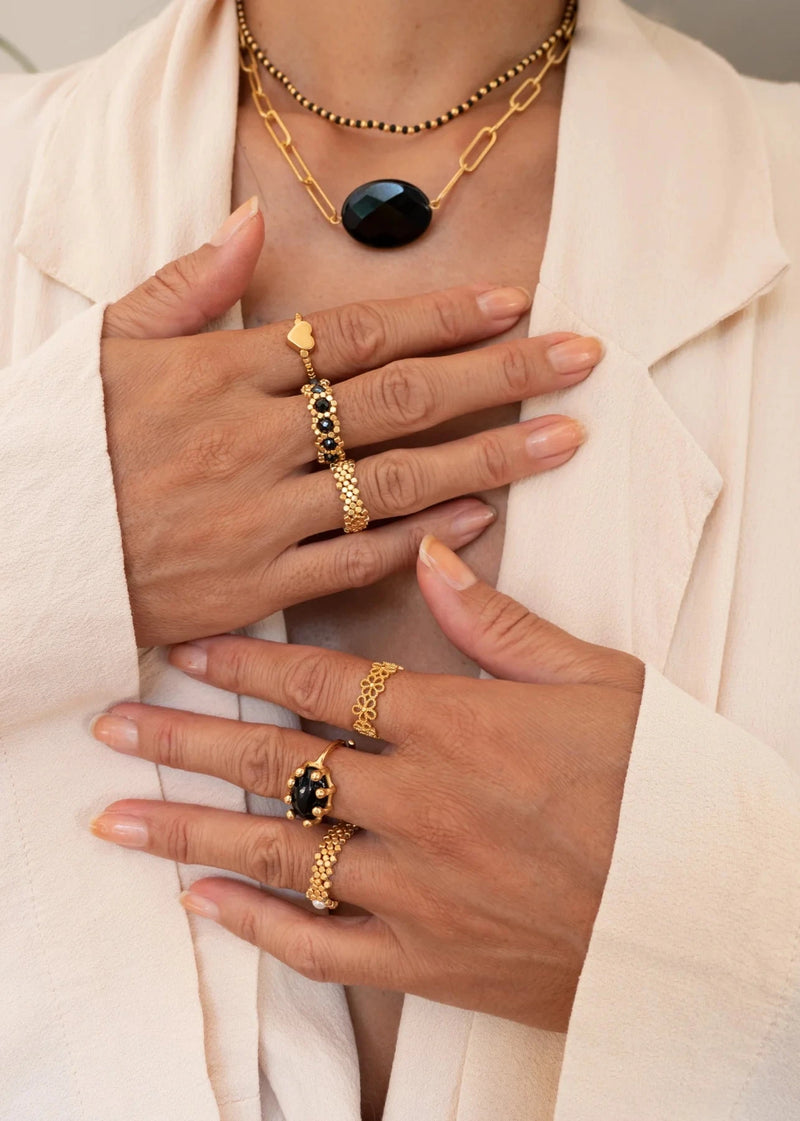 woman wearing black and gold jewellery with rings and multiple necklaces