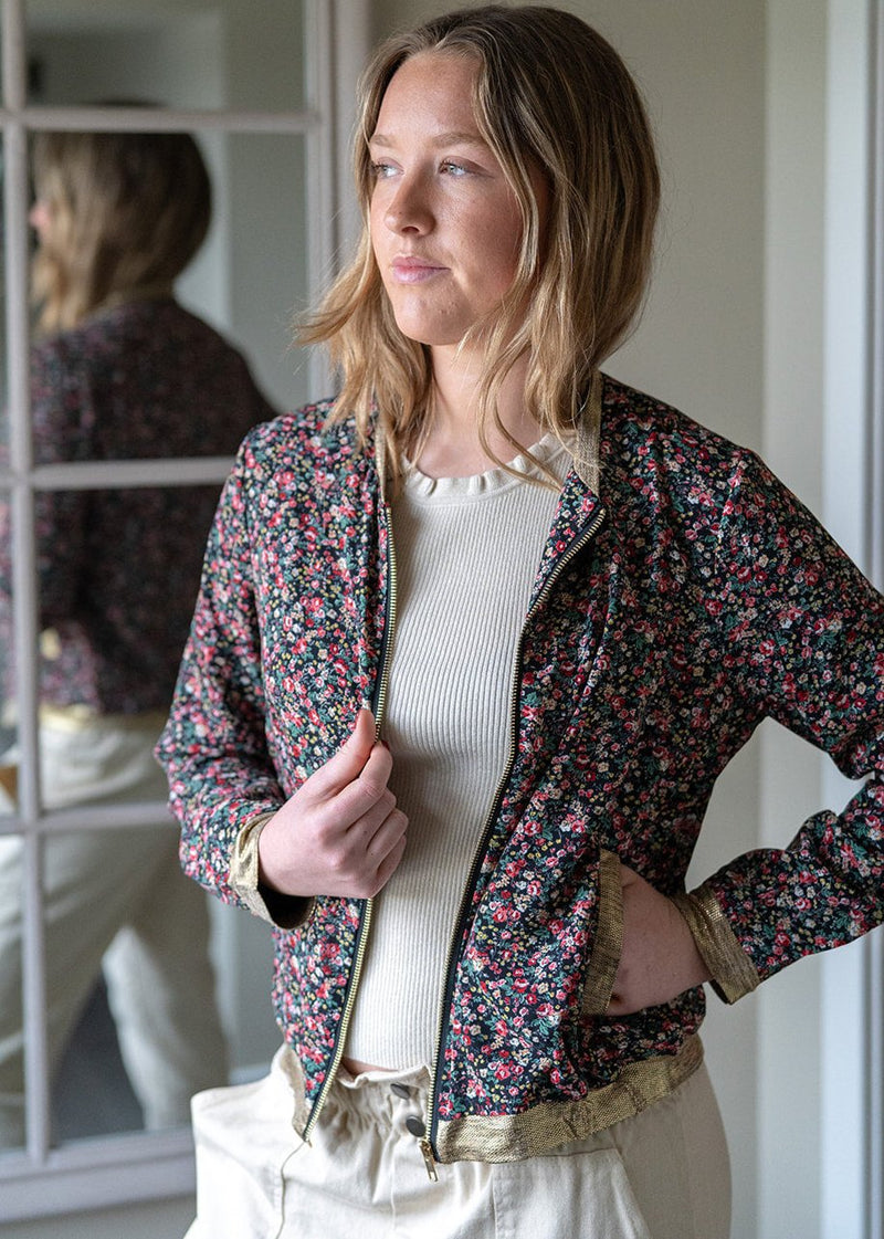 woman wearing the Matilda Silky Bomber Jacket / Top - Dark Ditsy with gold trim which has a multicoloured floral pattern on a black base colour. Tiny flower pattern