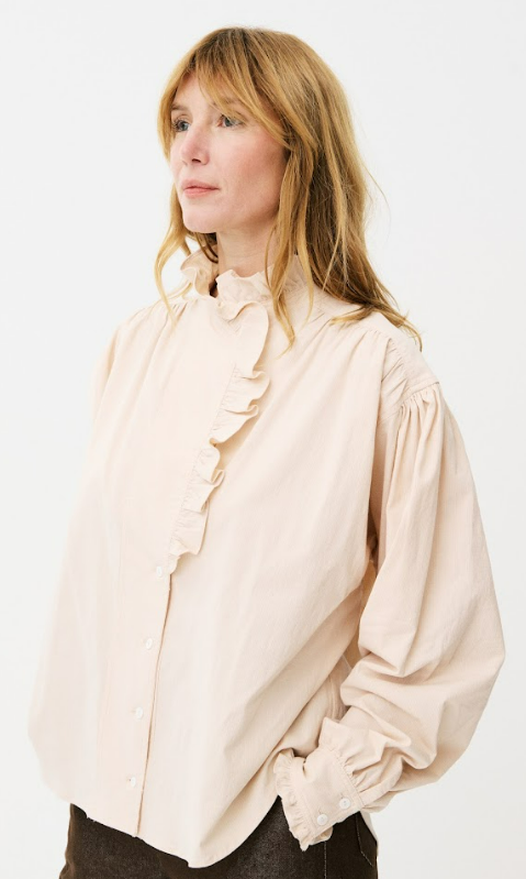 Woman wearing a light pink blouse with ruffled collar on a white background